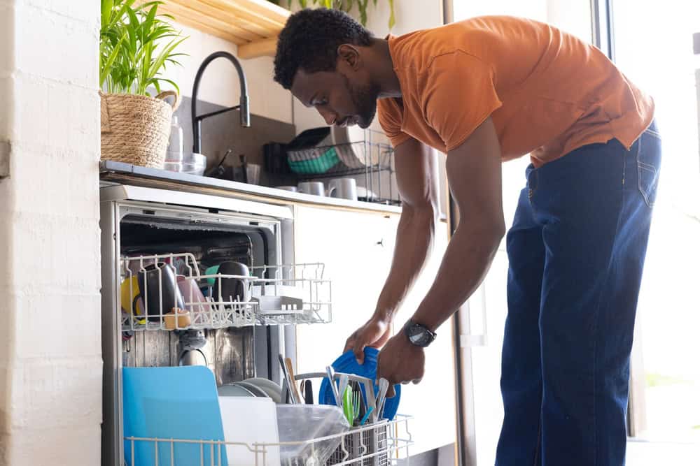 A man loads colorful dishes into a dishwasher in a bright, modern kitchen.