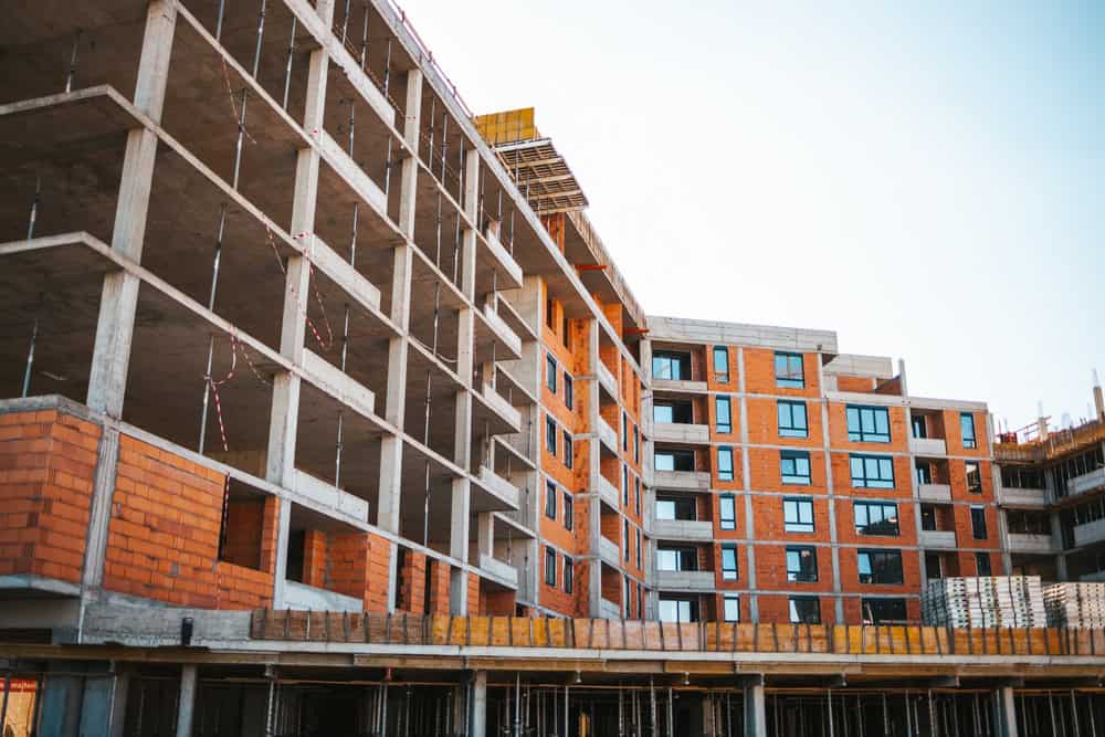 Urban apartments taking shape—concrete skeleton and red-brick facades under a clear sky.