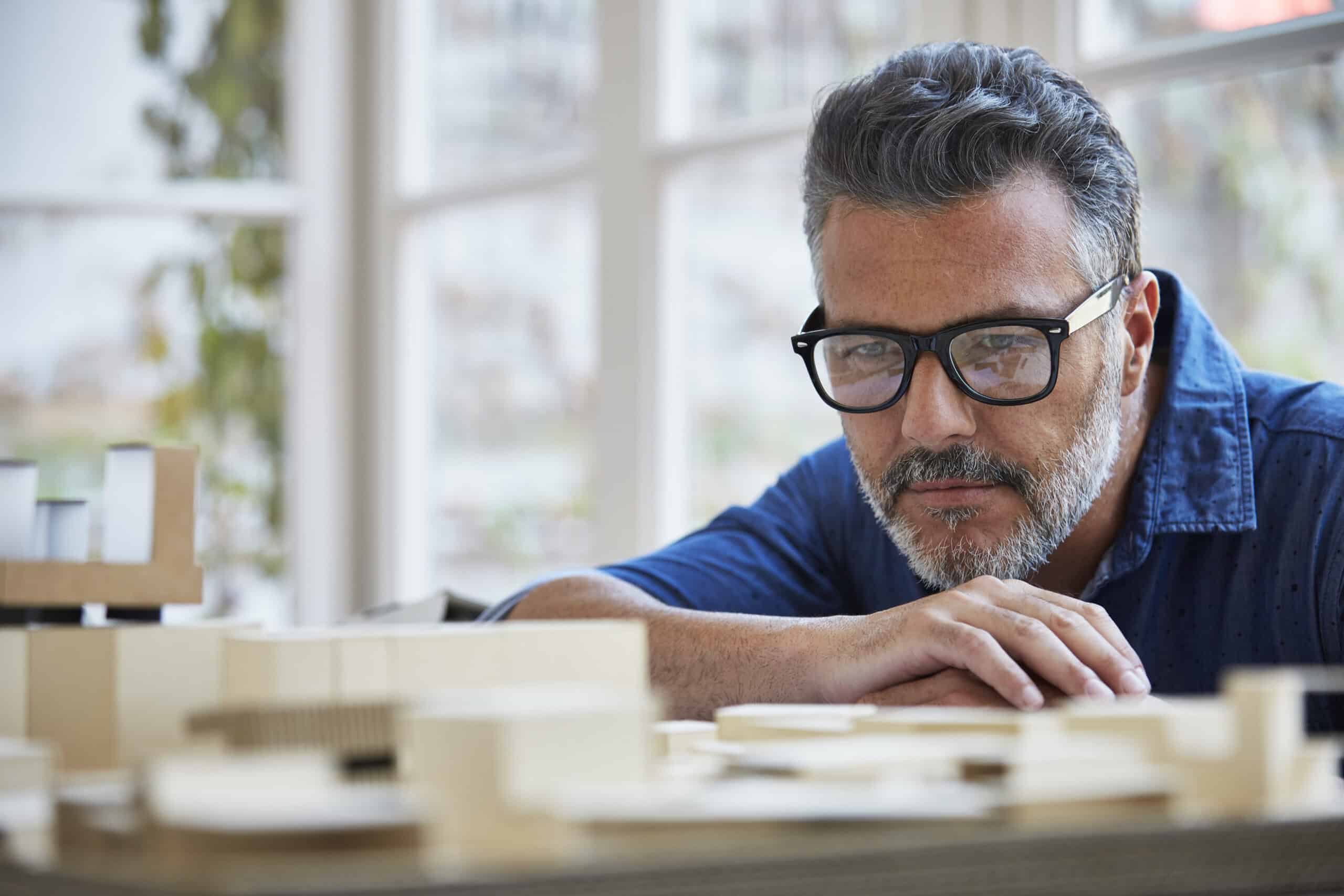 Architect looking at building model in office Mature male architect looking at building model in office