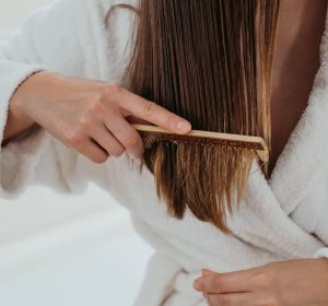 Unrecognised woman carefully combing her hair with a wooden comb. Closeup, Treatment for split ends hair.