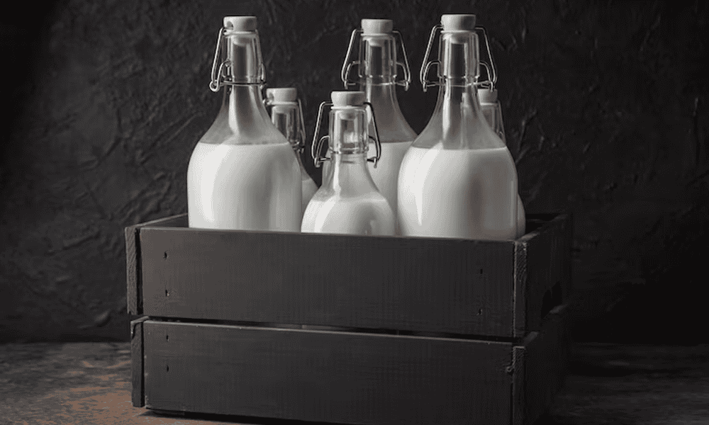 Stainless steel milk bottles with swing top caps in black wooden crate for dairy products.