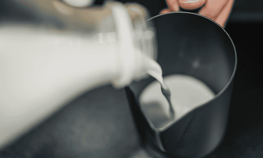 Fresh milk being poured into a black container, showcasing dairy equipment usage at NK Dairy Equipments.
