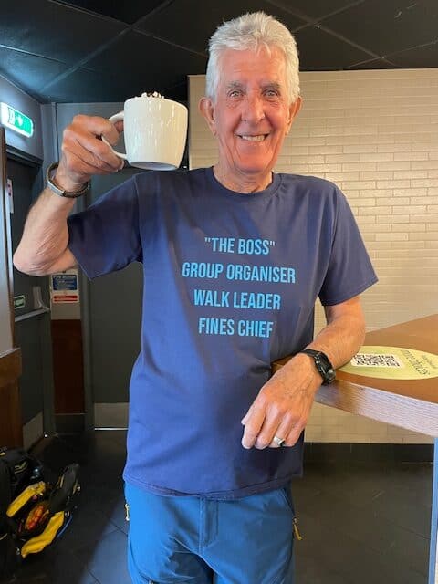 Smiling man holding mug, wearing role description T-shirt.
