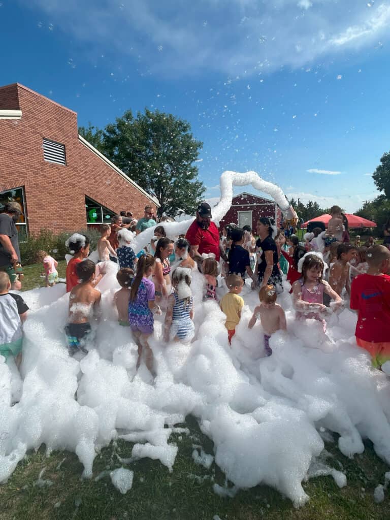 Kids having fun in a foam party with bubbles on a sunny day at northernplainspl.org, showcasing community events and outdoor activities.