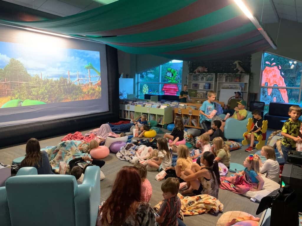 Animated children’s storytime and movie event at Northern Plains Public Library, featuring kids enjoying a colorful screen, cozy seating, and a vibrant, engaging environment.