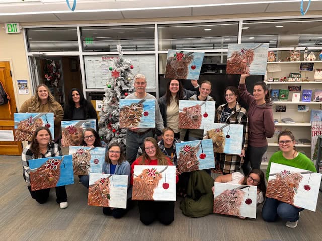 Kids and adults holding finished Christmas tree paintings in a festive indoor setting, celebrating holiday art projects at northernplainspl.org.