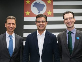 Camisa branca com blazer azul, homem de óculos, na frente de painel com símbolo do Brasil e bandeiras europeias, discurso político, congresso ambiental, reunião de líderes, evento internacional.