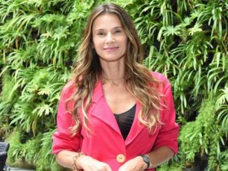 Mulher sorridente com cabelo liso e longo, usando blazer rosa, em ambiente com vegetação tropical exuberante, promovendo sustentabilidade e sustentabilidade ambiental.