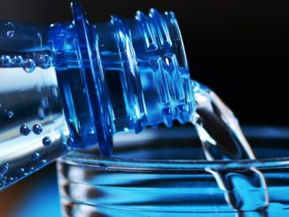 Água engarrafada sendo despejada em um copo, destaque para o líquido transparente e as bolhas.