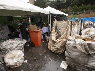 Reciclagem de resíduos sólidos urbanos em feira ecológica; equipe organizando materiais recicláveis sob toldo em evento de conscientização ambiental.