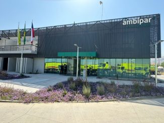 Ambipar Environmental escritório com veículos de emergência refletidos no vidro. Edifício moderno, paisagismo com flores e bandeiras ao vento, representando sustentabilidade e gestão ambiental eficiente.