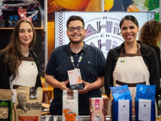 Coffe farm products at trade fair, with smiling booth staff and display of organic cacao and coffee items for sale.
