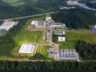 Industrial complex surrounded by greenery, with multiple buildings, parking areas, and access roads, highlighting environmental management and sustainable industrial practices.