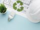 Vaso com planta próxima a lâmpada de LED, plano de fundo com plantas e projeto de construção, simbolizando sustentabilidade e inovação em construções ecológicas.