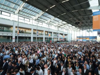 Milhares de pessoas participando de evento corporativo em grande aviação, com ambiente moderno e iluminação natural, promovendo networking e oportunidades de negócios na área de sustentabilidade.