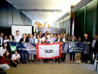 Municírio de ambientalismo, sustentabilidade e participação em evento ambiental com diversas pessoas sorridentes segurando bandeiras de apoio às causas ambientais e sociais.