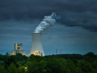 Central termoelétrica emitindo fumaça escura ao ar, cercada por vegetação, evidenciando impacto ambiental e necessidade de fontes de energia mais sustentáveis.