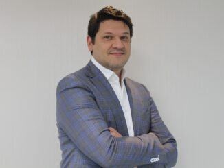 Homem de traje azul com expressão confiante posando com braços cruzados, background branco, enfatiza profissionalismo e credibilidade em notícias ambientais e comerciais.