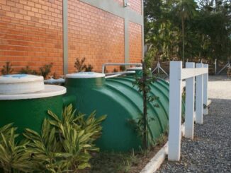 Tanque de armazenamento de água ecológico em ambiente externo, próximo a parede de tijolos, plantas verdes ao redor, ideal para sustentabilidade e gestão de recursos hídricos.