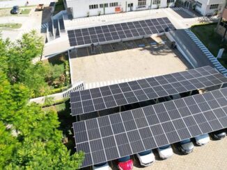 Painel solar fotovoltaico em estacionamento empresarial com árvores ao lado e edifícios modernos, promovendo sustentabilidade e economia de energia.