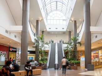 Passarela de shopping center com escadas rolantes e plantas decorativas, ambiente moderno e bem iluminado, ambiente comercial, ambiente de compras, ambientação de shopping center, localização de lojas.