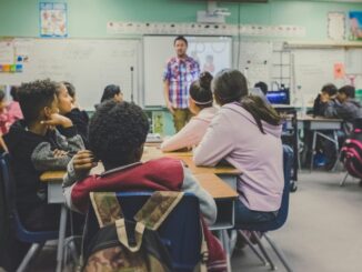 Estudantes assistindo à aula em sala de aula escolar, com professor na lousa, promovendo educação ambiental e aprendizagem sobre sustentabilidade.