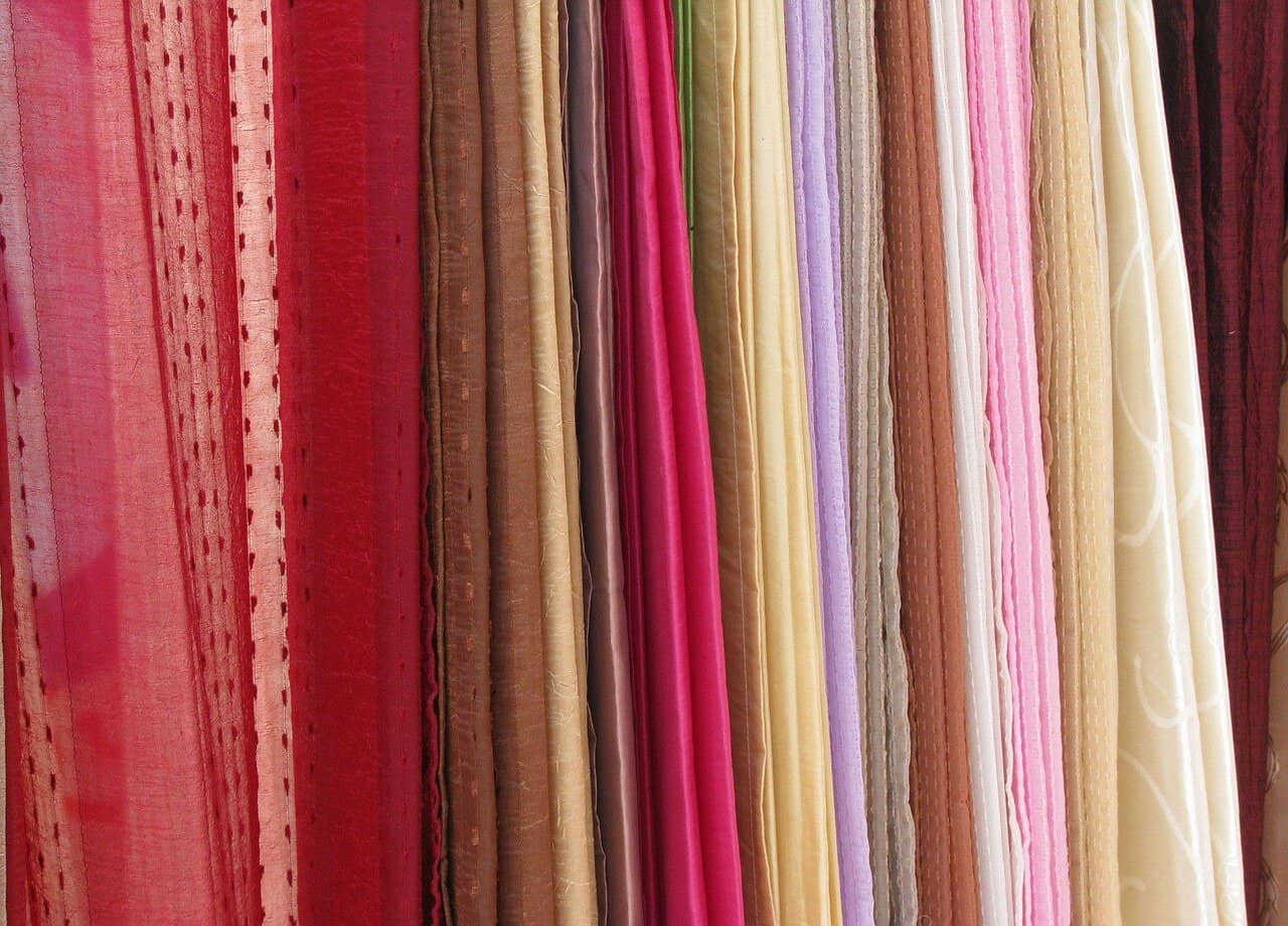 Fitas de cetim coloridas e variadas em tons de vermelho, rosa, lilás, amarelado, bege e branco, em uma mostra de tecidos para decoração, moda ou artesanato.