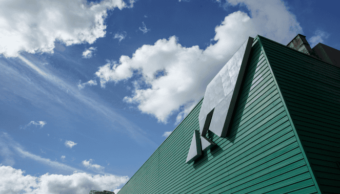 Sede da Ambiental Mercantil com destaque para o logotipo em uma fachada moderna sob céu azul com nuvens.