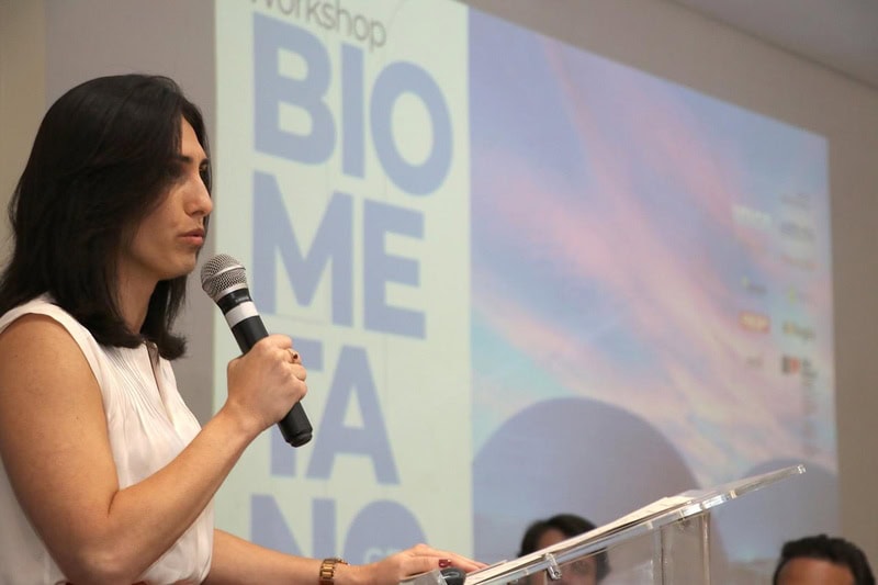 Convença mulher falando sobre biomimética em workshop ambiental, com tela ao fundo exibindo o tema bio mimética, destacando inovação sustentável e ecoeficiência na preservação ambiental.