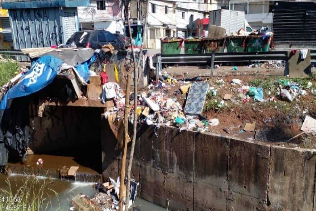 Poluição urbana, lixo acumulado em canal de escoamento pluvial, descarte de resíduos sólidos, ambiente urbano degradado, lixo e sujeira na cidade, problemas ambientais e saneamento precário.