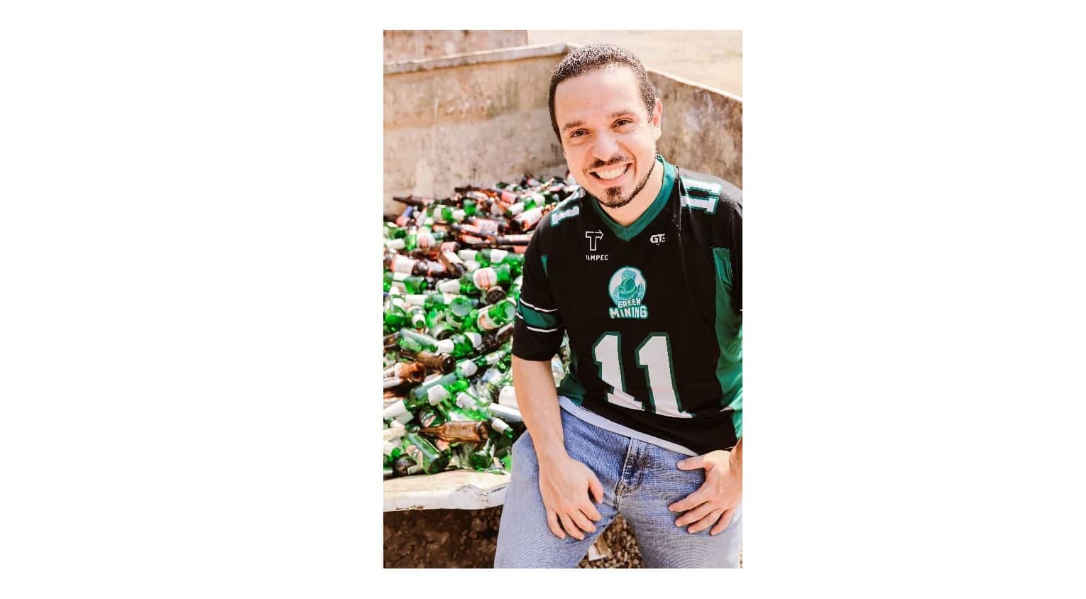 Garoto sorridente com camisa esportiva de sustentabilidade, ao lado de pilhas de garrafas plásticas recicladas, promovendo ações ambientais e reciclagem para preservação do meio ambiente.
