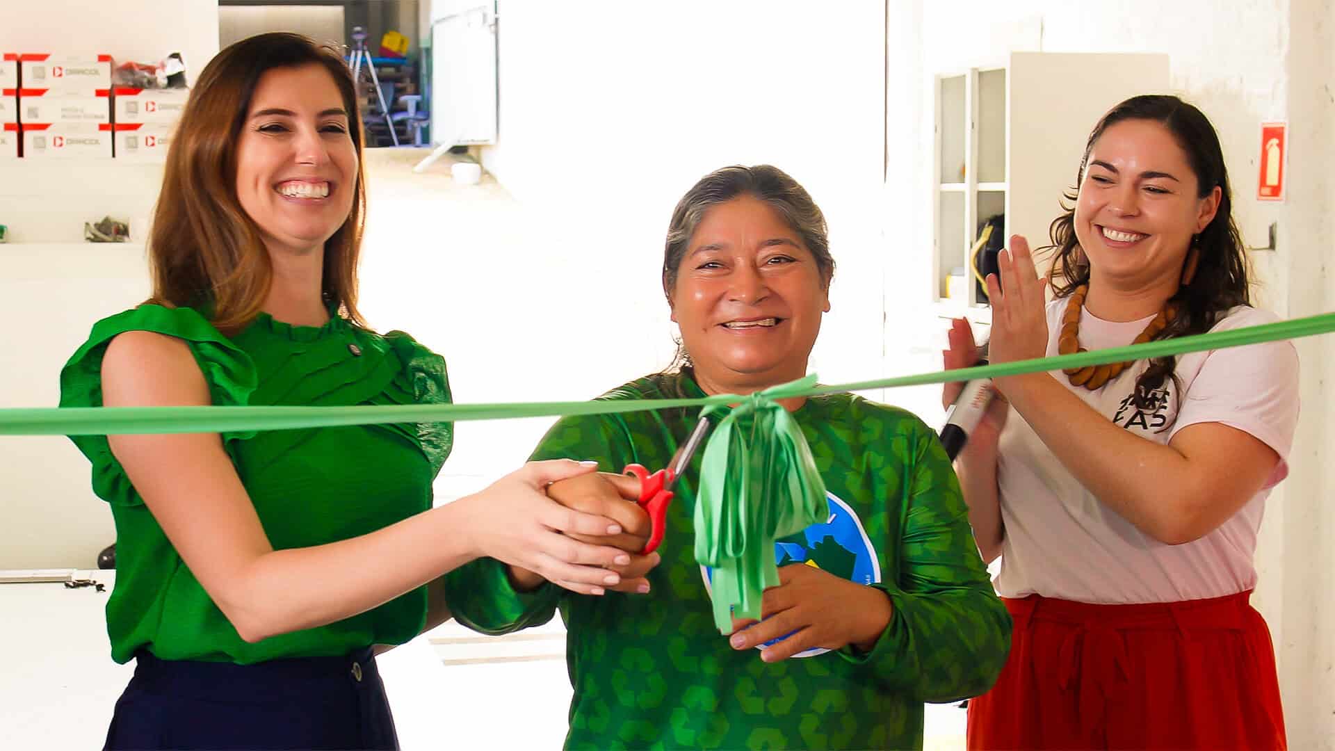 Artesãs celebrando a inauguração de espaço sustentável com uma fita de corte verde, símbolo de compromisso ambiental e sustentabilidade, promovendo projetos de preservação ambiental e ações ecológicas.