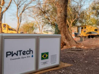 Tanque de captação de água da PWTech com logotipo, ambiente ao ar livre, árvores e veículos ao fundo, promovendo soluções sustentáveis para gestão de recursos hídricos e meio ambiente.