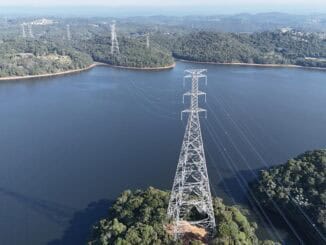 Linhas de transmissão de energia elétrica sobre reservatório com árvores ao redor, refletindo a importância de infraestrutura sustentável no setor energético.