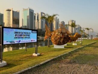 Painel digital de sustentabilidade ambiental em área urbana com edifícios modernos ao fundo, promovendo conscientização sobre economia circular e proteção ambiental na região.