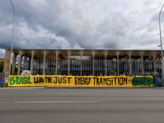 Brasil, protesto pelo uso de energia limpa e transição energética, na frente de edifício governamental, com faixa destacando liderança na transição energética no COP30.