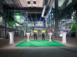Tanque de armazenamento de resíduos industriais na fábrica com iluminação especial e equipe de trabalhadores em vestimenta de segurança, promovendo sustentabilidade e inovação no setor ambiental.