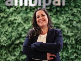 Profissional sorridente em ambiente corporativo na Ambiental Mercantil, com fundo de parede verde e logo visível, transmitindo confiança e compromisso com sustentabilidade ambiental e negócios sustentáveis.