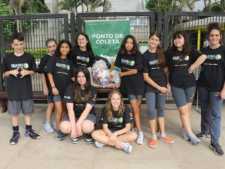 Estudantes participando de uma ação de coleta de materiais recicláveis em frente a um ponto de coleta ambiental.