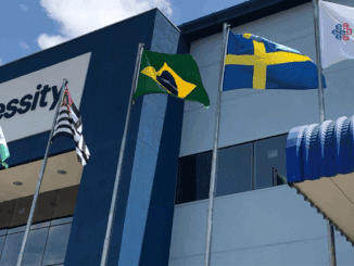 Edifício da Ambiental Mercantil com bandeiras do Brasil, Suécia, Goiás e uma bandeira do programa Esprit. Fachada moderna com céu azul ao fundo, destacando presença internacional e forte relacionamento empresarial.