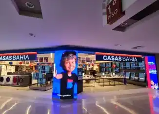 Loja de eletrodomésticos Casas Bahia em um centro de compras, com uma grande tela digital exibindo uma mulher sorridente e o logo da loja, promovendo produtos e ofertas para consumidores.