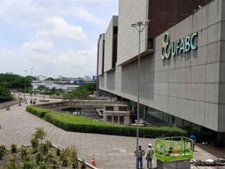 Fachada moderna do prédio do UFABC com área de circulação ao ar livre, equipe de manutenção trabalhando e paisagismo bem cuidado na cidade de São Paulo.