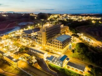 Fábrica industrial com iluminação noturna, destacando infraestrutura moderna e sustentável em região de desenvolvimento econômico.