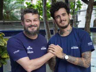 Homens sorridentes usando camisetas com logotipo do movimento Vozes dos Oceanos, representando engajamento ambiental e preservação marinha.