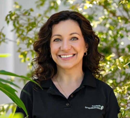 Mulher sorridente com cabelo cacheado e blusa preta, ao ar livre, promovendo sustentabilidade e responsabilidade ambiental.
