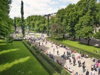 Pessoas desfrutando de um parque urbano com áreas verdes, árvores abundantes e bancos ao ar livre, criando um ambiente relaxante e sustentável na cidade.