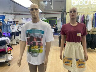Mannequins vestindo roupas masculinas e femininas em loja de moda casual, com destaque para camisetas com estampas coloridas e peças de vestuário em um ambiente de shopping, promovendo tendências de moda sustentável e conforto.