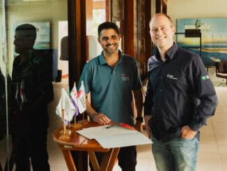 Documentos de negócios sendo assinados por dois homens sorridentes em ambiente corporativo, destacando parceria e acordos comerciais, com símbolos de sustentabilidade ambiental e crescimento empresarial.