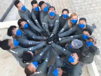 Grupo de profissionais usando máscaras em formação de círculo, simbolizando trabalho em equipe e comprometimento com segurança ambiental.