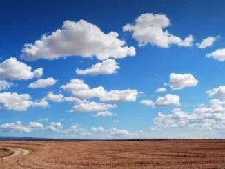 Nuvens brancas no céu azul sobre um vasto campo de terra árida, destacando a importância da preservação ambiental e do equilíbrio ecológico.